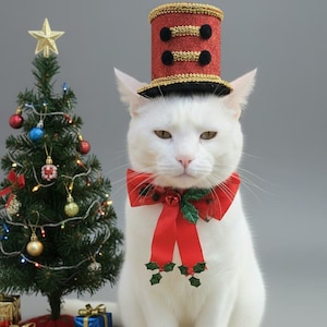 May include: A white cat wearing a red and gold hat and a red bow tie with holly accents, posing in front of a small Christmas tree decorated with ornaments and a star. Several wrapped gifts are at the base of the tree.