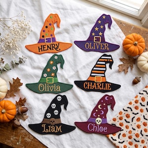 May include: Six embroidered witch hat patches featuring various designs and names. The hats are orange with polka dots, purple with stars, green with flowers, black and orange stripes, black with skulls, and maroon with moons and a skull, labeled with names.