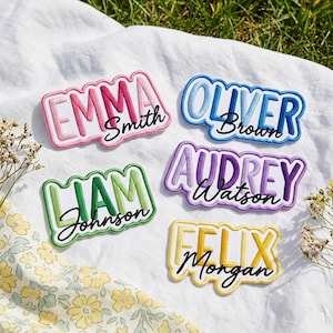 May include: Five rectangular embroidered patches with scalloped edges, each featuring a first name in large block letters and a last name in black cursive script. The patches are colour-coded in pink, blue, green, purple, and yellow gradients.