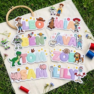 Op de afbeelding: Acht gepersonaliseerde geborduurde naamlabels met Toy Story-figuren. De namen LEO, MIA, BEN, AVA, TOM, ZOE, SAM en LILY zijn in pasteltinten geborduurd met thema-iconen zoals Woody, Buzz Lightyear, Bo Peep, Rex, Slinky Dog, Hamm en Forky.