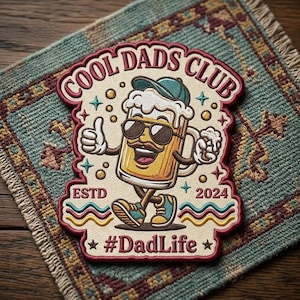 Può includere: Toppa ricamata con la scritta "COOL DADS CLUB" e un boccale di birra dei cartoni animati con occhiali da sole e berretto. La toppa include la scritta "ESTD 2024" e "#DadLife" su uno sfondo decorativo.