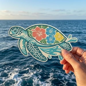 May include: A sea turtle patch featuring a teal and white patterned body with a shell decorated with a large coral hibiscus, two blue hibiscus flowers, and one yellow hibiscus flower, all surrounded by green leaves and stylized water splashes.
