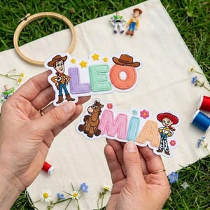 Puede incluir: Dos parches de tela bordados con personajes de Toy Story. Un parche muestra el nombre LEO en letras pastel con Woody y estrellas amarillas. El segundo parche muestra el nombre MIA en letras pastel con Perdigón y Jessie.
