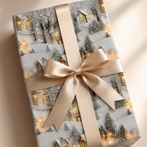 May include: A rectangular gift box wrapped in paper featuring a winter village scene with snow-covered houses and evergreen trees. The package is tied with a wide, smooth, champagne-colored satin ribbon arranged in a classic cross-pattern bow.