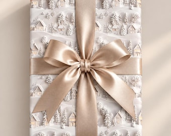May include: A rectangular gift box wrapped in white paper featuring a repeating pattern of embossed snowy hills, evergreen trees, and small houses. The package is tied with a wide, smooth, metallic champagne-colored satin ribbon bow.