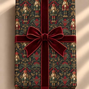 May include: A rectangular gift box wrapped in dark paper featuring a repeating pattern of nutcracker figures and ornate floral motifs in red, green, and gold. A wide, deep red velvet ribbon is tied in a large bow across the centre.