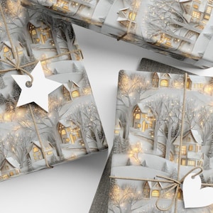 May include: Three rectangular gift boxes wrapped in white paper featuring a winter village scene with snow-covered houses, bare trees, and warm glowing lights. Each package is tied with brown twine and includes a white paper gift tag.