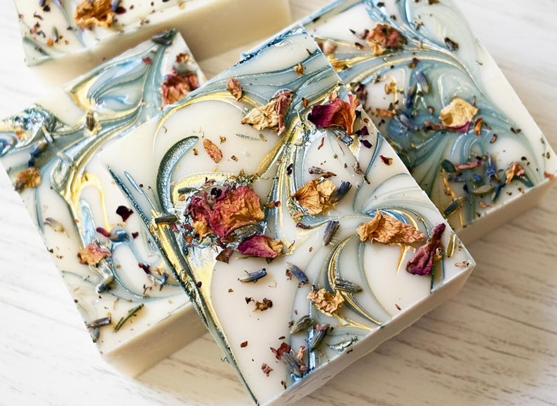 Custom designed soap favors with a dusty blue and gold mica swirl top and dried botanicals
