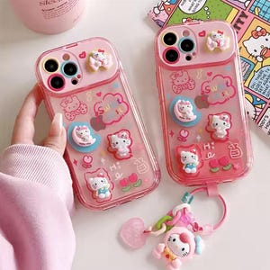 Può includere: Una custodia per telefono rosa e trasparente con personaggi e disegni di Hello Kitty. La custodia ha un anello porta-dito integrato e un retro trasparente che mostra il colore del telefono. La custodia ha anche un ciondolo rosa Hello Kitty.