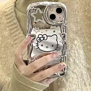May include: A silver phone case featuring a Hello Kitty design and a glittery background. The case has a raised border and a clear back.