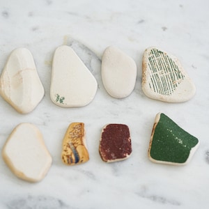 May include: Eight ceramic tiles with various designs. Some tiles are white with green and brown markings, while others have green, brown, and yellow designs.