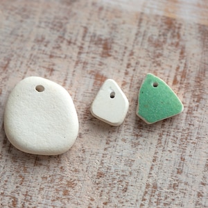 May include: Three ceramic pendants with holes for hanging. The pendants are white and green, and have irregular shapes.
