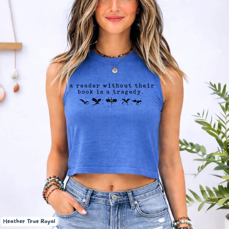 May include: A blue crop top with the text "a reader without their book is a tragedy." and four black silhouette images. The shirt is a heather true royal color.