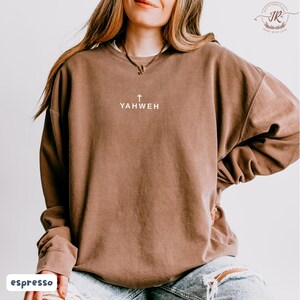 May include: Espresso-colored sweatshirt with the word "YAHWEH" printed in white, above a small cross. The sweatshirt has a crew neck and long sleeves. The word "espresso" is printed in a white box at the bottom left.