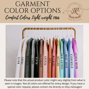 May include: A display of t-shirts in various colors, including white, grey, black, and vibrant hues like neon violet and blue jean. The text "GARMENT COLOR OPTIONS" and "Comfort Colors Light weight 1466" are visible. The shirts hang on a gold rack.