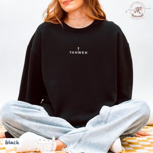May include: Black crewneck sweatshirt with the word "YAHWEH" and a cross printed in white. The sweatshirt is a solid black color. The word "black" is printed at the bottom left corner of the image.