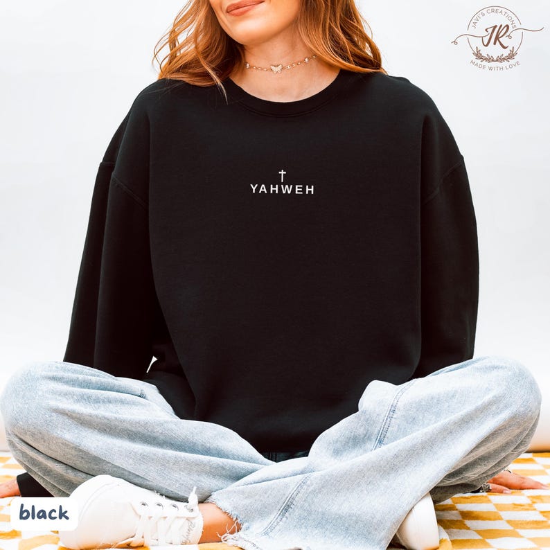 May include: Black crewneck sweatshirt with the word "YAHWEH" and a cross printed in white. The sweatshirt is a solid black color. The word "black" is printed at the bottom left corner of the image.