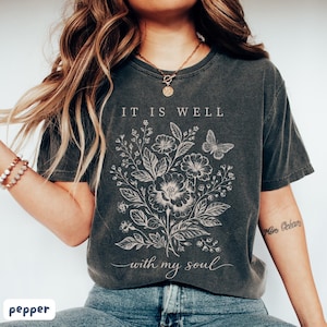 May include: Dark grey t-shirt featuring the text "IT IS WELL with my soul" and a white floral and butterfly design. A comfortable, casual style.