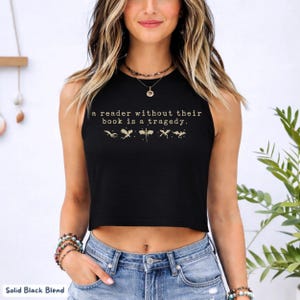 May include: Black crop top with the quote "a reader without their book is a tragedy." The text is in a light tan color, with small illustrations below the text. The shirt is a solid black blend.