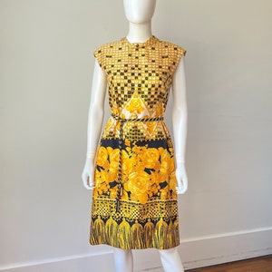 May include: A sleeveless dress with a black and yellow geometric pattern and floral print. The dress has a black belt and a fringe hem.