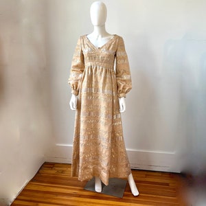 May include: A long, gold-colored dress with a V-neck and long sleeves. The dress has a metallic silver pattern and a fitted bodice.