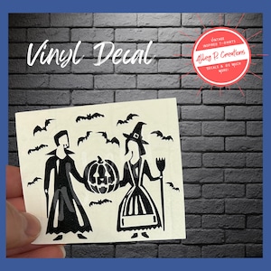 May include: A black and white vinyl decal featuring a Halloween theme. The decal shows a vampire and a witch holding a carved pumpkin, with bats flying above. The text "Vinyl Decal" is at the top.