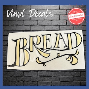 May include: A white vinyl decal with the word "BREAD" in a vintage-inspired font. The letters are outlined in black with a yellow fill. The decal also features decorative flourishes and the text "Vinyl Decals".