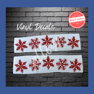 May include: Two sets of red snowflake vinyl decals. Each set contains five snowflakes. The words "Vinyl Decals" are at the top of the image. A circular logo in the upper right corner reads "Alley R Creations".