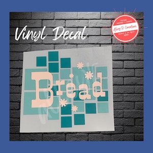 May include: A vinyl decal featuring the word "Bread" in a light peach hue, set against a backdrop of teal and turquoise squares and snowflake shapes. The words "Vinyl Decal" are above the design.