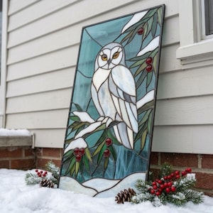 Peut inclure: Un panneau rectangulaire en vitrail représentant un hibou blanc perché sur une branche enneigée avec des feuilles vertes et des baies rouges. Le fond est d'un bleu sarcelle froid, le tout encadré par un bord en métal sombre et des lignes de plomb.