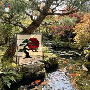 May include: A square stained glass panel featuring a black bonsai tree silhouette against a large, deep red circular sun, set against a cream-colored background with wavy horizontal lines, all enclosed within a thin, dark metal frame.