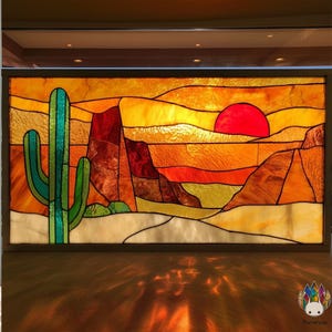 Puede incluir: Panel de vidrieras que representa un paisaje desértico con una puesta de sol. La obra presenta un cactus verde, formaciones rocosas rojas y un gran sol rojo contra un cielo amarillo y naranja. El panel está enmarcado en un borde marrón oscuro.