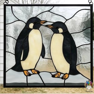 Könnte beinhalten: Buntglasfenster mit zwei Pinguinen. Die Pinguine haben einen schwarzen Rücken, einen weißen Bauch und orangefarbene Schnäbel und Füße. Der Hintergrund ist ein strukturiertes, hellgraues Glas. Das Panel ist schwarz gerahmt und hat eine Aufhängekette.