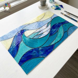 Op de afbeelding: Een rechthoekig glas-in-loodstuk dat oceaangolven in tinten blauw, turquoise en wit afbeeldt. Het glas is gesegmenteerd met donkere lijnen, waardoor een mozaïekeffect ontstaat. Het ontwerp roept de zee op.
