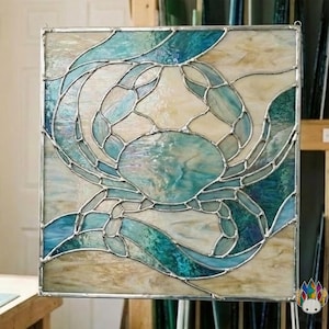 May include: Stained glass panel featuring a crab design. The crab is rendered in shades of blue and teal, with a textured appearance. The background is a mix of off-white and tan, with wavy blue accents. The panel is framed with a silver metal border.
