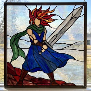 May include: A square stained glass panel featuring a figure with flowing red and orange hair, wearing a blue tunic and a green scarf. The figure holds a large silver sword. The background consists of clear textured glass with red ground.