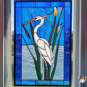 May include: Stained glass panel depicting a white heron in a watery scene with reeds. The heron has an orange beak, set against a blue backdrop with water and sky details. The panel is framed with a dark blue border.