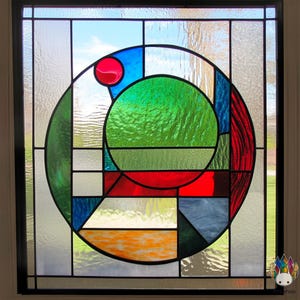 Peut inclure: Une fenêtre en vitrail avec un motif circulaire composé de formes géométriques dans des tons de rouge, vert, bleu et orange.