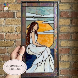 Peut inclure: Panneau en vitrail représentant une femme en robe blanche, assise devant un coucher de soleil. L'œuvre est encadrée dans un métal foncé, avec une palette de couleurs bleue et orange. Le panneau est rectangulaire et contient le texte "COMMERCIAL LICENSE".
