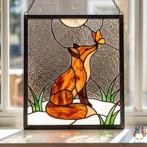 May include: Stained glass panel featuring a fox and butterfly. The fox is orange and white, with a butterfly in shades of orange and yellow. The background is a textured gray with a moon and stars. The panel is framed in black.