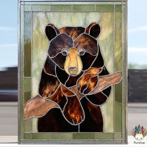 May include: Stained glass panel featuring a brown bear with a yellow snout and paws, holding a branch. The bear is set against a light green background within a rectangular frame. The artwork is a decorative piece.