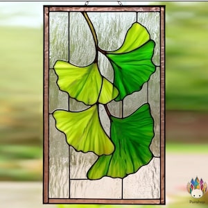 May include: Stained glass panel featuring a ginkgo leaf design. The leaves are rendered in shades of green and yellow, with dark brown stems and a textured background. The panel is framed in a dark brown border and is suitable for window decor.
