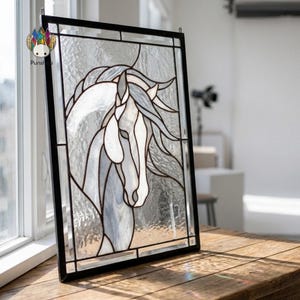 Könnte beinhalten: Glasfenster mit einem weißen Pferdekopf und fließender Mähne, umrahmt von Schwarz. Das Design befindet sich vor einem strukturierten Glas Hintergrund. Das Panel wird auf einer Holzoberfläche in der Nähe eines Fensters präsentiert.
