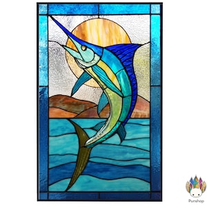 May include: Stained glass panel featuring a leaping marlin against a backdrop of a sun and ocean waves. The marlin is depicted in shades of blue, green, and yellow, with a long, pointed bill. The panel is framed in a dark blue border.