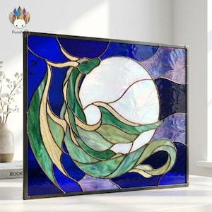 Peut inclure: Un panneau rectangulaire en vitrail représentant la silhouette d'un dragon vert enroulé devant une grande lune circulaire blanche irisée. L'arrière-plan se compose de segments de verre bleu profond et violet, assemblés par des lignes de plomb.