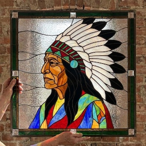 May include: A square stained glass panel featuring a profile portrait of a person wearing a traditional feathered headdress. The design uses vibrant red, blue, yellow, and green glass pieces, set within a dark green frame with clear textured glass.