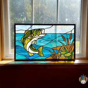 May include: Stained glass panel depicting a leaping fish in green, white, and yellow against a blue water backdrop. The artwork includes cattails and a shoreline, framed in black. A decorative piece for home decor.