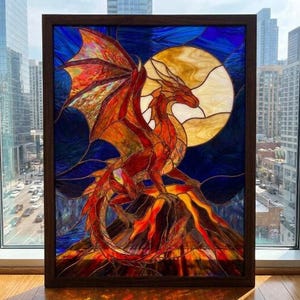 Può includere: Un pannello in vetro colorato rettangolare in una cornice di legno scuro raffigurante un drago rosso e arancione appollaiato su una cima vulcanica contro una grande luna piena giallo pallido. Lo sfondo presenta segmenti di vetro blu.