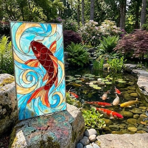 Peut inclure: Un panneau rectangulaire en vitrail représentant une carpe koï rouge foncé nageant au milieu de motifs en verre bleu clair et crème. Le panneau est encadré de métal et présente un design vibrant et translucide qui laisse passer la lumière.