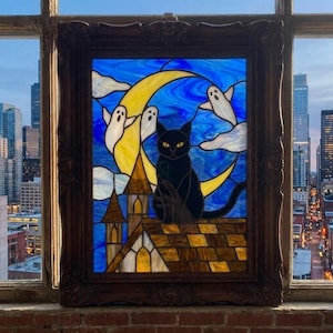 Op de afbeelding: Een glas-in-loodpaneel in een donkerhouten lijst met een zwarte kat op een bruin pannendak. Achter de kat staat een grote gele maansikkel tegen een blauwe lucht met witte geesten en wolken. Het paneel is geplaatst in een raamkozijn.